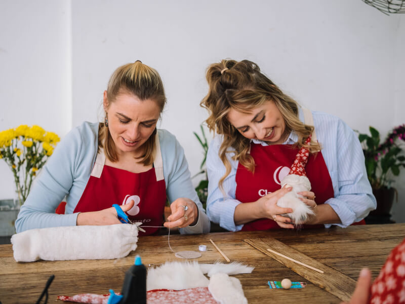 Two women wearing red aprons making Christmas crafts